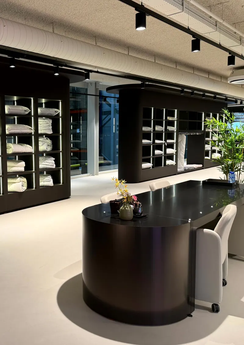 Der Showroom von HMG: ein schwarzer Tisch vor beleuchteten Wandregalen mit Kissen und Bettdecken